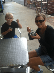 Caleb and his mum are sitting outside on a cafe table enjoying liquorice ice cream.